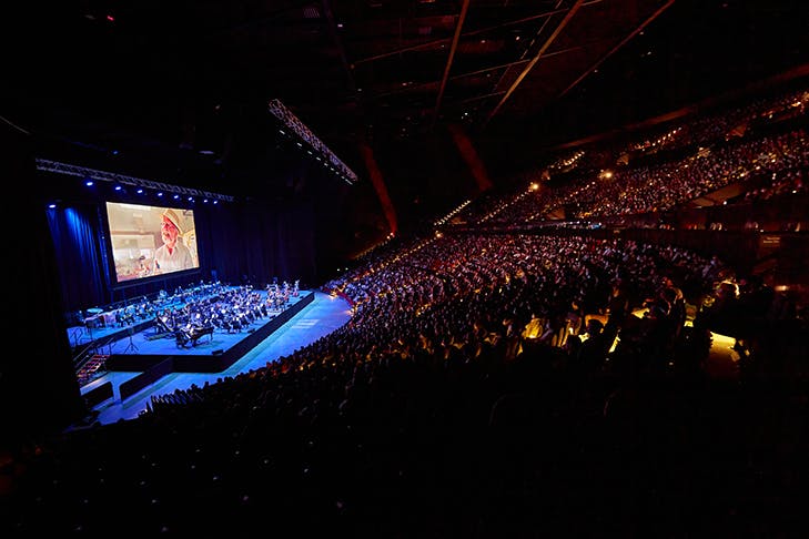 An orchestra playing in front of giant screen.